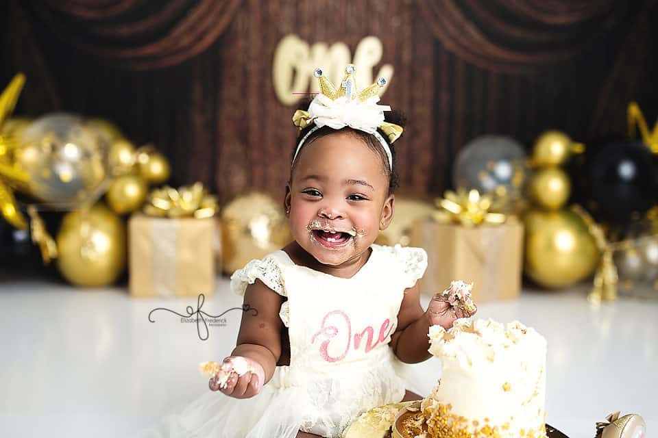 New Year’s Day smash cake session featuring a one-year-old baby girl with a gold and black backdrop photographed by a CT smash cake photographer.